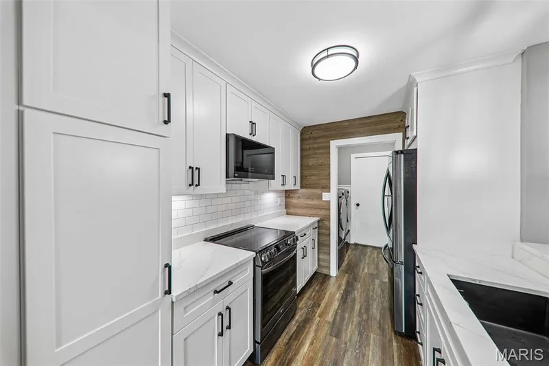 Modern kitchen featuring white shaker cabinetry with matte black hardware, white subway tile backsplash, light-toned countertops, and wood-finish flooring — 16180 Lea Oak Court, Chesterfield, MO 63017