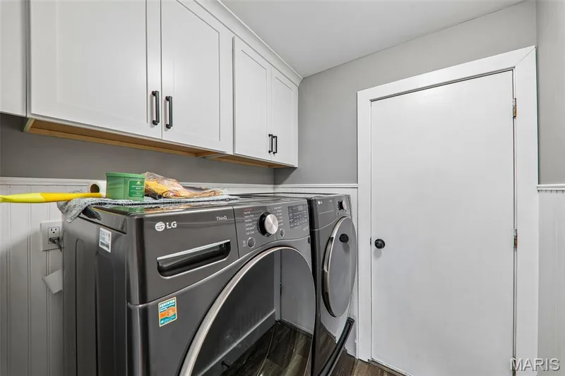 Laundry area featuring overhead white shaker-style cabinetry with dark hardware, white beadboard wainscoting, and wood-finish flooring — 16180 Lea Oak Court, Chesterfield, MO 63017