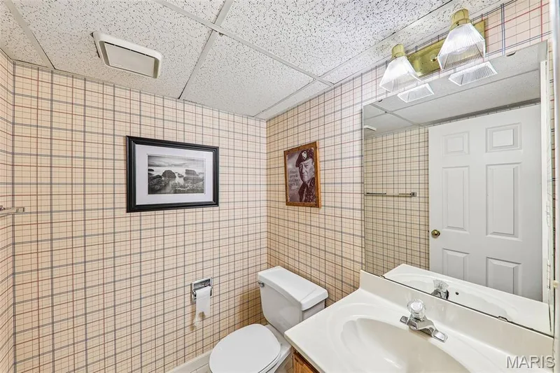 Bathroom featuring a drop ceiling with recessed lighting, patterned wallpaper, a white vanity with an integrated sink, a large wall-mounted mirror, and a standard toilet — 16180 Lea Oak Court, Chesterfield, MO 63017