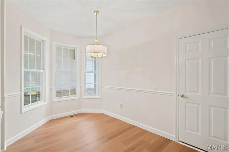 Bay window featuring three double-hung windows, wood-finish flooring, chair rail molding, a neutral color palette, and a drum-style chandelier — 704 Harrier Drive #V, Lake St. Louis, MO 63367