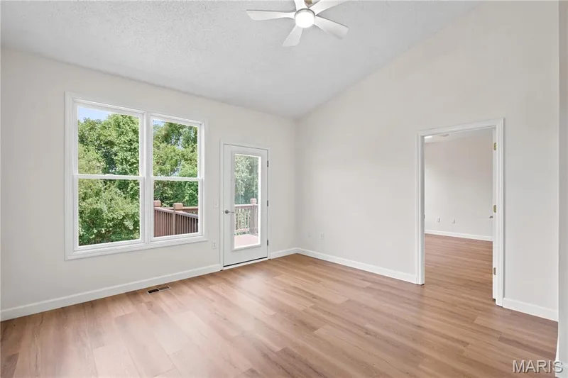 Vaulted ceiling room featuring wood-finish flooring, white trim, a ceiling fan, and access to an exterior deck — 704 Harrier Drive #V, Lake St. Louis, MO 63367