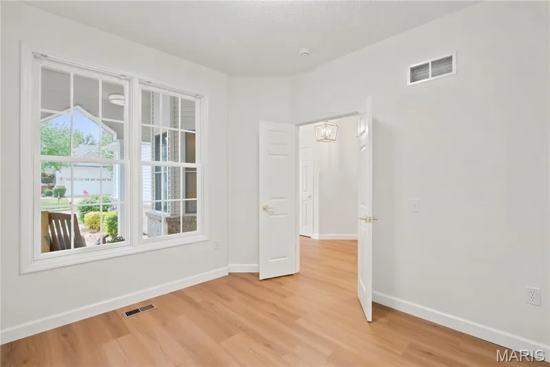 Light-filled interior space featuring wood-finish flooring, white trim, and a double window with grids — 704 Harrier Drive #V, Lake St. Louis, MO 63367