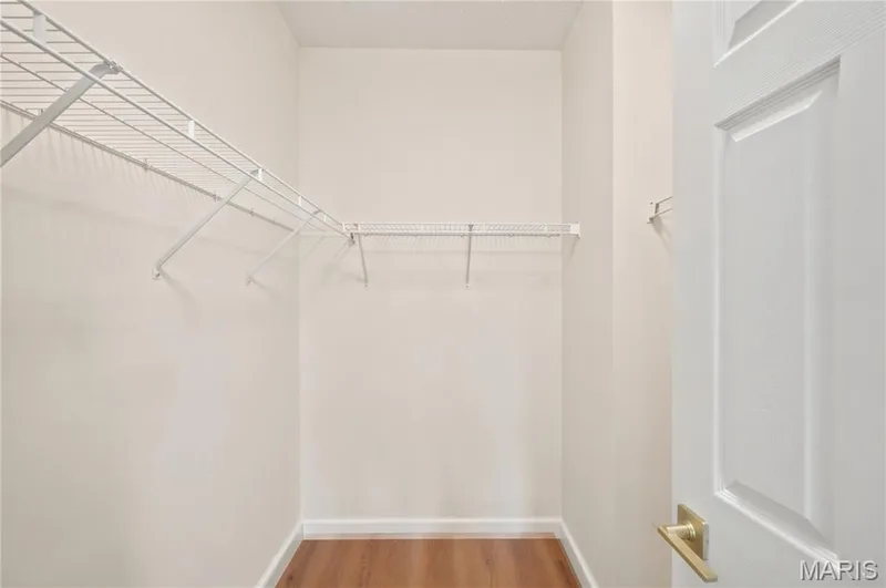 Recessed closet featuring white wire shelving, light neutral walls, wood-finish flooring, and a white panel door with brass hardware — 704 Harrier Drive #V, Lake St. Louis, MO 63367