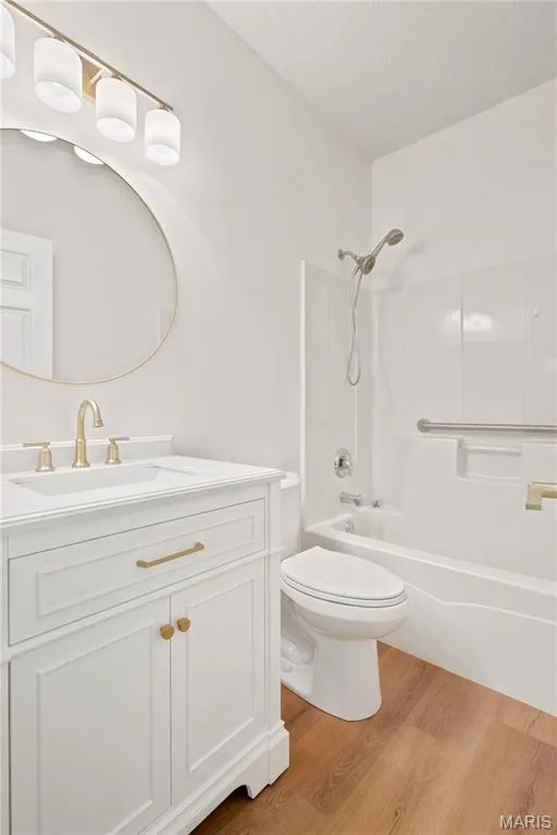 White vanity with gold-tone hardware, a circular mirror, and a three-light vanity fixture — 704 Harrier Drive #V, Lake St. Louis, MO 63367