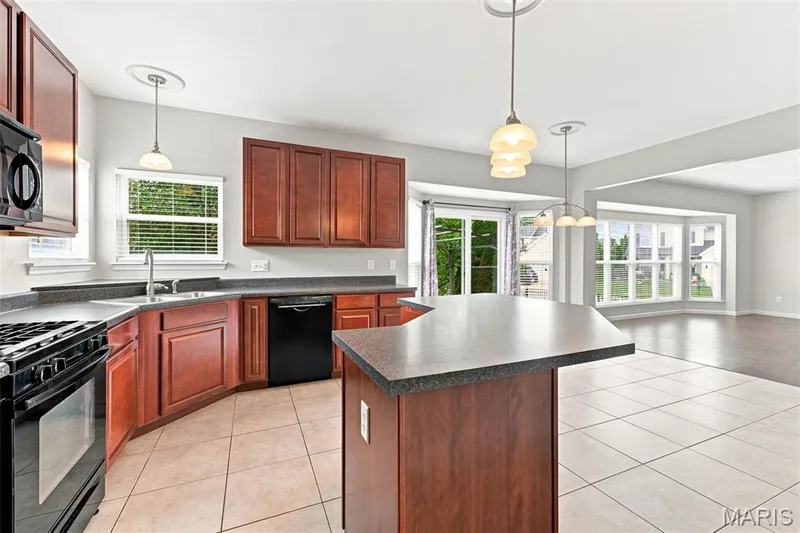Spacious open kitchen featuring rich wood cabinetry, center island, abundant counter space, pantry, and black appliances. Sunny breakfast room with sliding glass doors to the patio flows seamlessly into the expansive great room, creating the perfect layout for entertaining and everyday living. Large windows provide an abundance of natural light throughout. — 104 Towergate Drive, Lake St. Louis, MO 63367