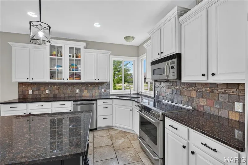 The Kitchen features white 42" Cabinetry with crown molding, Stainless Steel appliances, and granite countertops with tile backsplash. — 31 Pinewood Court, Dardenne Prairie, MO 63368