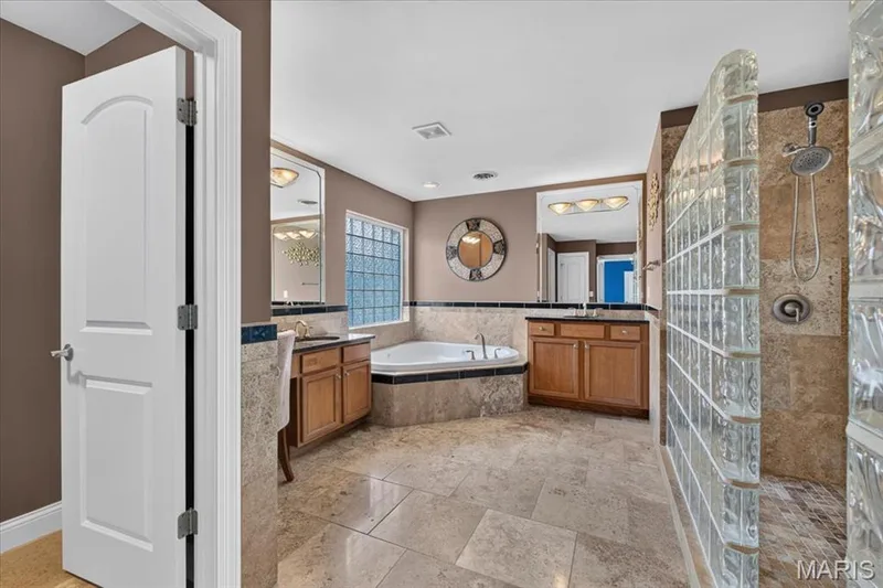 The Primary En Suite Bath includes a walk in block shower with tile surround, his and her vanities and large corner jet tub. — 31 Pinewood Court, Dardenne Prairie, MO 63368