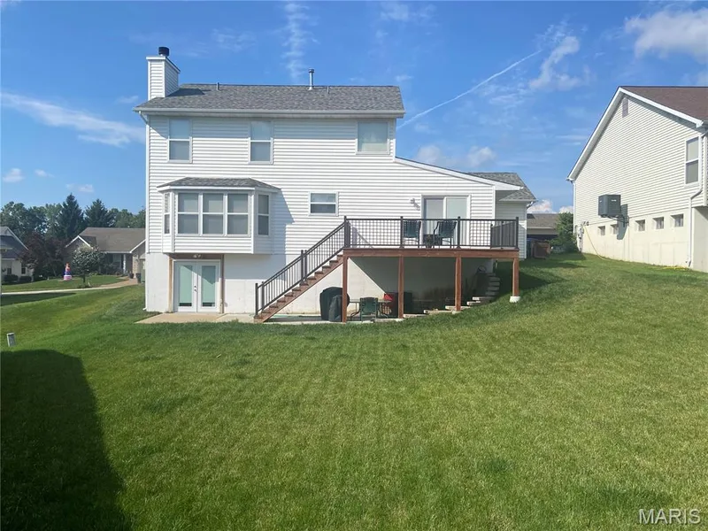 Rear exterior featuring white vinyl siding, a bay window, and a ground-level patio with double glass doors — 1113 Treeshade Drive, St Peters, MO 63376