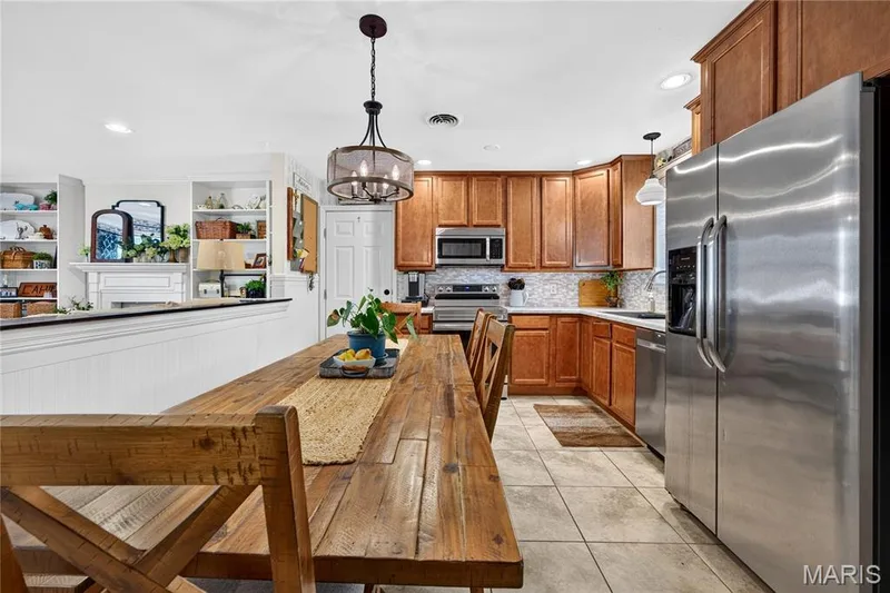 Open-concept kitchen featuring wood cabinetry, stainless steel appliances, and a mosaic tile backsplash — 802 Barbara Place, O'Fallon, MO 63366