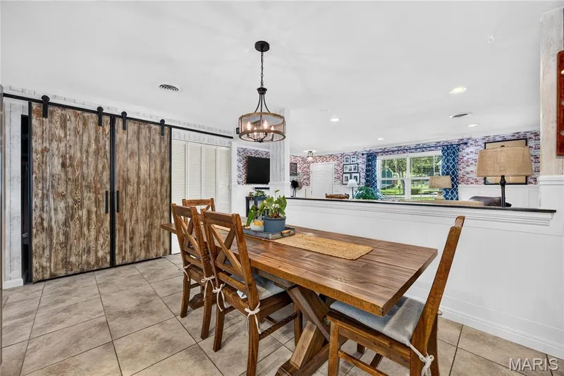 Dining area featuring plank-style sliding barn doors, tile flooring, a decorative chandelier, and a half-wall partition — 802 Barbara Place, O'Fallon, MO 63366