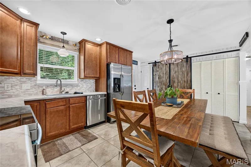 Kitchen and dining area featuring wood-finish cabinetry, stainless steel appliances, a tile backsplash, and a window over the sink — 802 Barbara Place, O'Fallon, MO 63366
