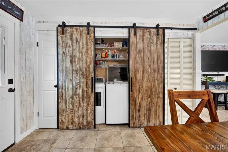 Barn door style enclosure featuring a laundry area with built-in shelving, tile flooring, and white paneled walls — 802 Barbara Place, O'Fallon, MO 63366