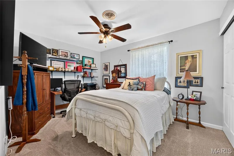 Carpeted interior room featuring a ceiling fan with light fixture, a window with sheer curtains, a built-in closet with sliding doors, and wall-mounted shelving — 802 Barbara Place, O'Fallon, MO 63366