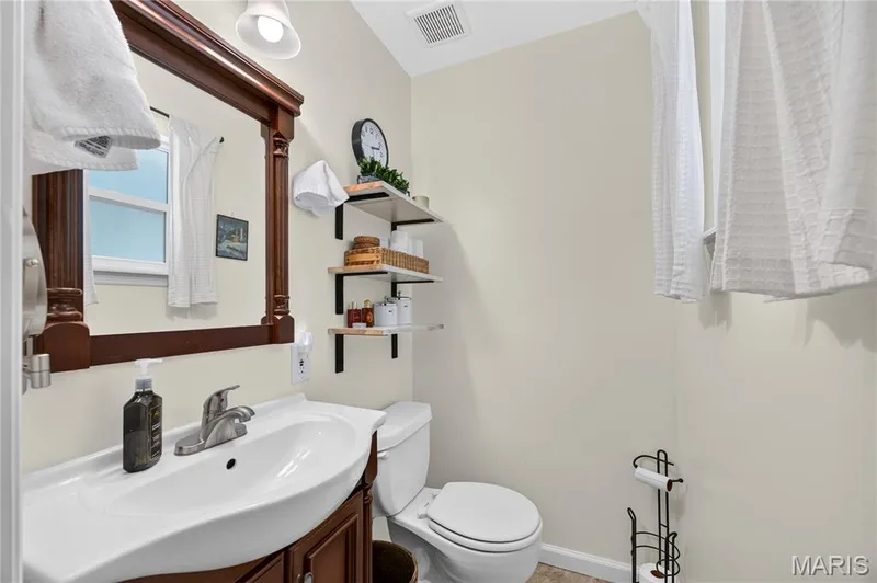 Bathroom featuring a dark wood-finish vanity with an integrated white sink, a matching framed mirror, and a toilet — 802 Barbara Place, O'Fallon, MO 63366