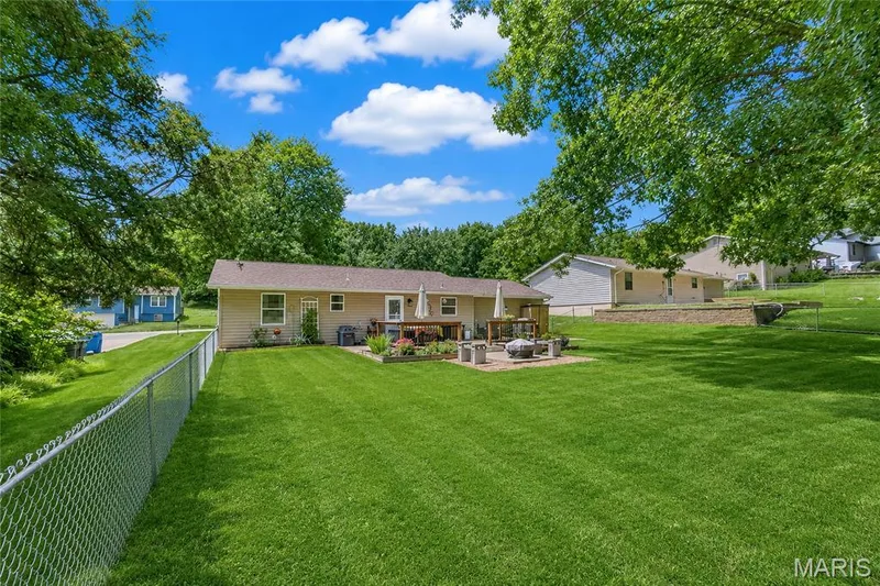 Expansive lawn area with a chain-link fence, mature trees, and a beige exterior — 802 Barbara Place, O'Fallon, MO 63366