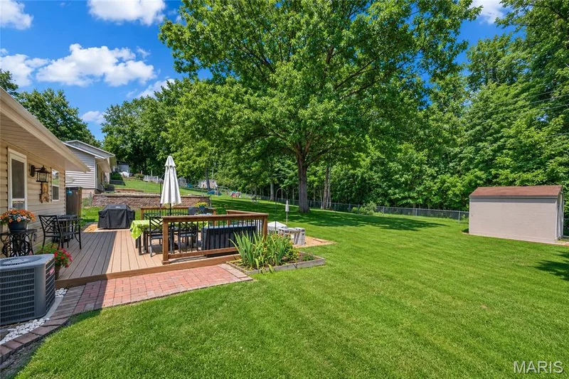 Expansive backyard featuring a large wood-finish deck, brick paver patio, a freestanding storage shed, and mature trees providing natural screening — 802 Barbara Place, O'Fallon, MO 63366