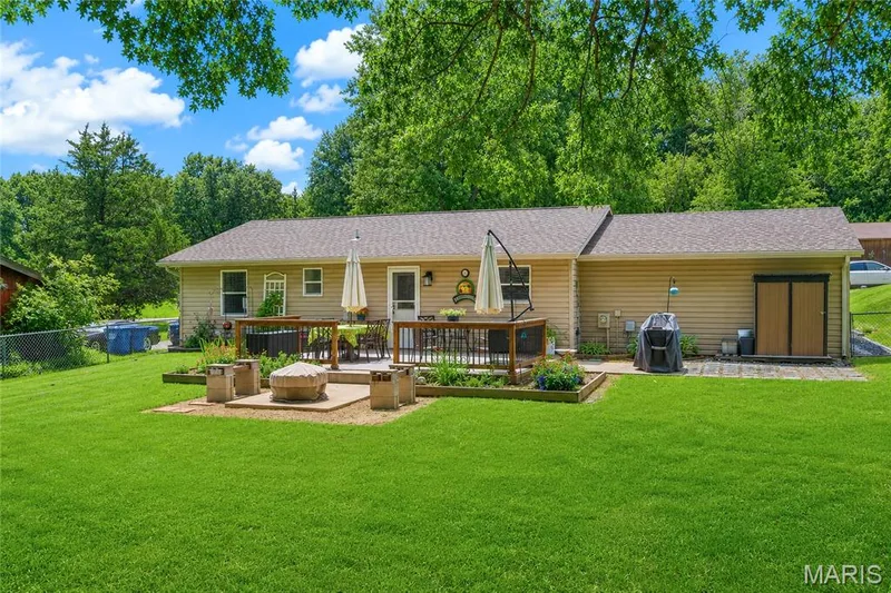 Expansive backyard featuring a large green lawn, a multi-level deck with wood railings, and a concrete paver patio — 802 Barbara Place, O'Fallon, MO 63366