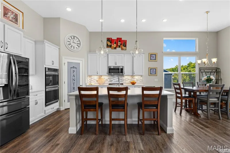 Open kitchen and living area with wood finish flooring and a kitchen island with seating. — 1316 Silver Fern Drive, Lake St. Louis, MO 63367