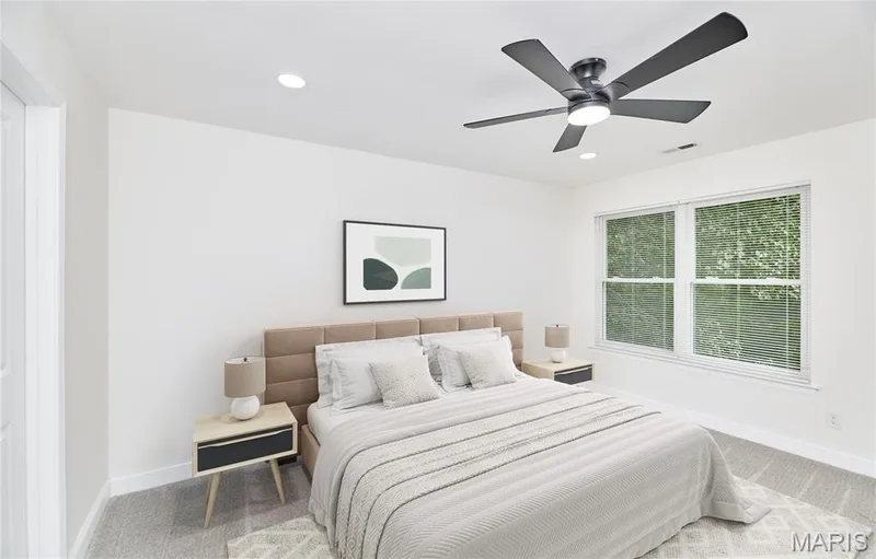 Spacious bedroom featuring light gray carpeting, crisp white walls, a contemporary ceiling fan with integrated lighting, recessed ceiling lights, and double-hung windows — 214 Sugar Lake Drive #5, St Peters, MO 63376