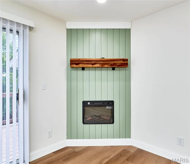 Built-in electric fireplace with a substantial wood mantel, set against a light green vertical panel accent wall — 214 Sugar Lake Drive #5, St Peters, MO 63376