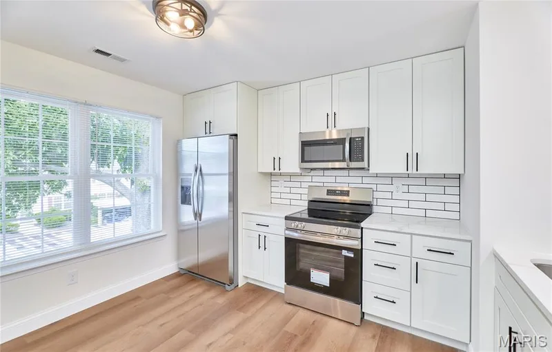 Kitchen featuring white shaker-style cabinetry with matte black hardware, stainless steel appliances, and wood-finish Luxury vinyl plank flooring — 214 Sugar Lake Drive #5, St Peters, MO 63376