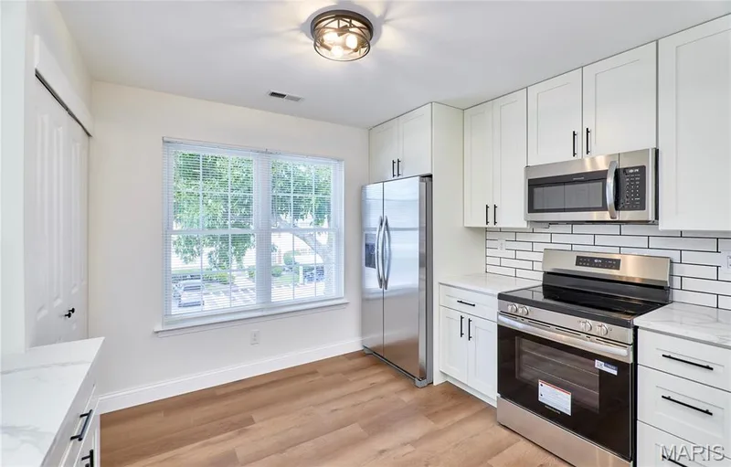 Kitchen featuring white shaker-style cabinetry with matte black hardware, stainless steel appliances, and wood-finish Luxury vinyl plank flooring, and white subway tile backsplash — 214 Sugar Lake Drive #5, St Peters, MO 63376