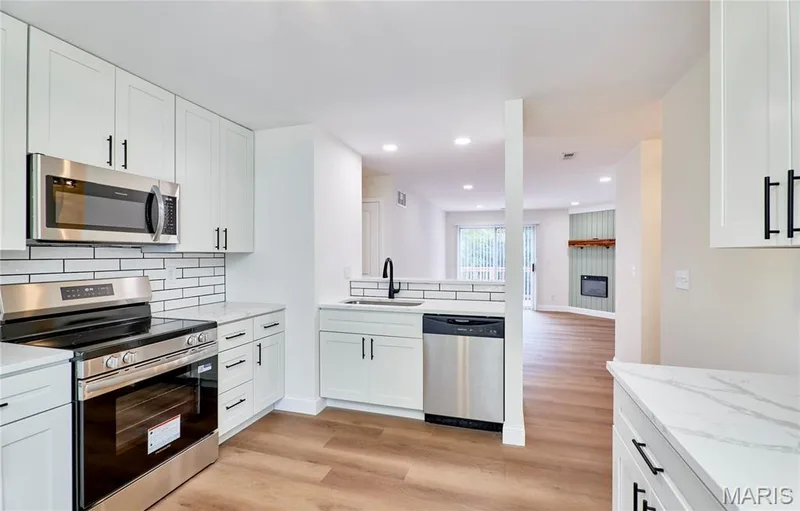 Modern kitchen featuring white shaker-style cabinetry with matte black hardware, stainless steel appliances, a subway tile backsplash, and light-colored countertops — 214 Sugar Lake Drive #5, St Peters, MO 63376
