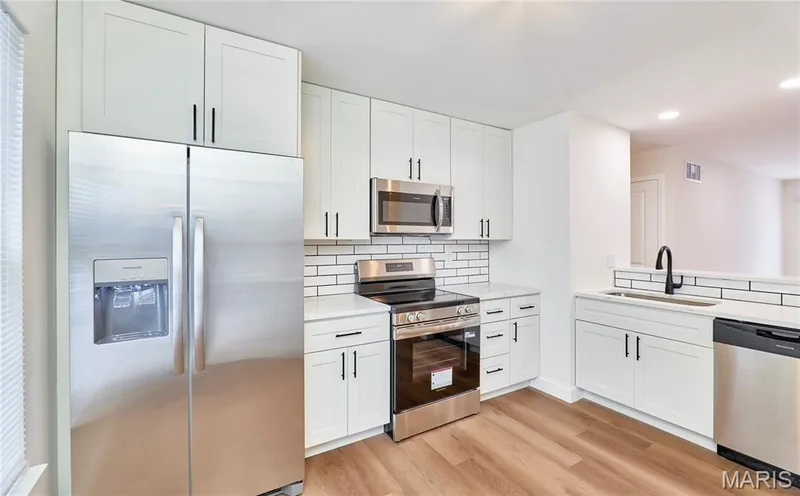 Modern kitchen featuring white shaker cabinetry, stainless steel appliances, white subway tile backsplash, and wood-finish Luxury vinyl plank flooring — 214 Sugar Lake Drive #5, St Peters, MO 63376