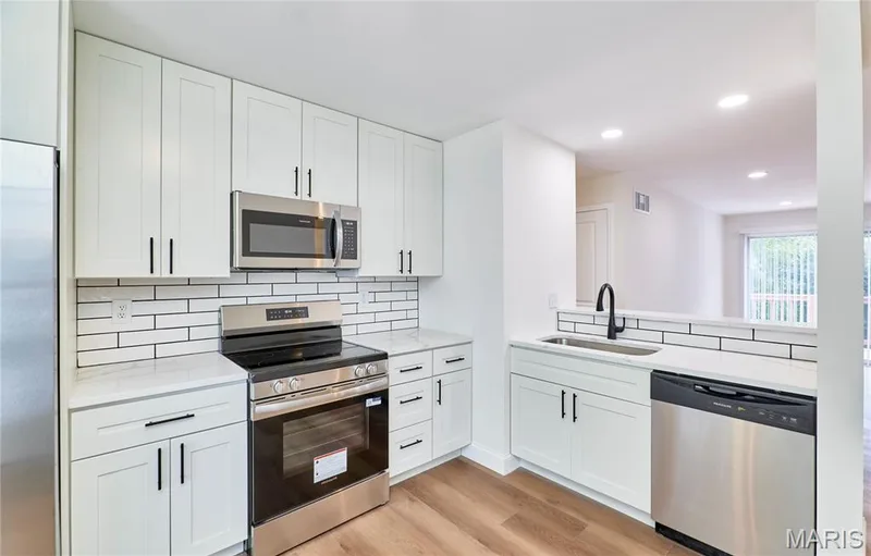 Modern kitchen featuring white shaker cabinetry, stainless steel appliances, white subway tile backsplash, and wood-finish Luxury vinyl plank flooring — 214 Sugar Lake Drive #5, St Peters, MO 63376