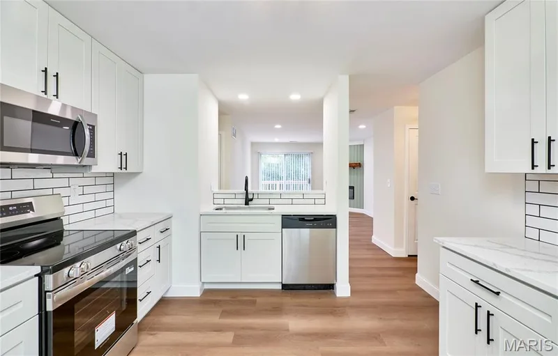 Kitchen featuring wood-finish Luxury vinyl plank flooring, white cabinetry with matte black hardware, white subway tile backsplash, and stainless steel appliances — 214 Sugar Lake Drive #5, St Peters, MO 63376