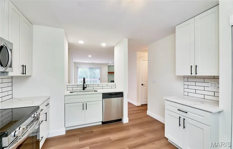 Bright kitchen featuring white shaker cabinetry, stainless steel appliances, a black faucet, white subway tile backsplash, and wood-finish Luxury vinyl plank flooring — 214 Sugar Lake Drive #5, St Peters, MO 63376