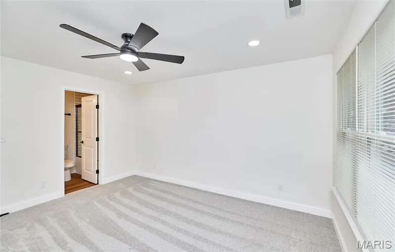 Spacious bedroom featuring light-colored carpeting, white baseboards, and a contemporary ceiling fan with integrated lighting — 214 Sugar Lake Drive #5, St Peters, MO 63376