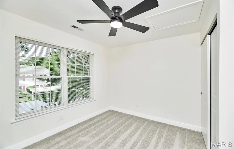 Light-filled bedroom featuring two double-hung windows, a ceiling fan with integrated lighting, plush gray patterned carpet — 214 Sugar Lake Drive #5, St Peters, MO 63376