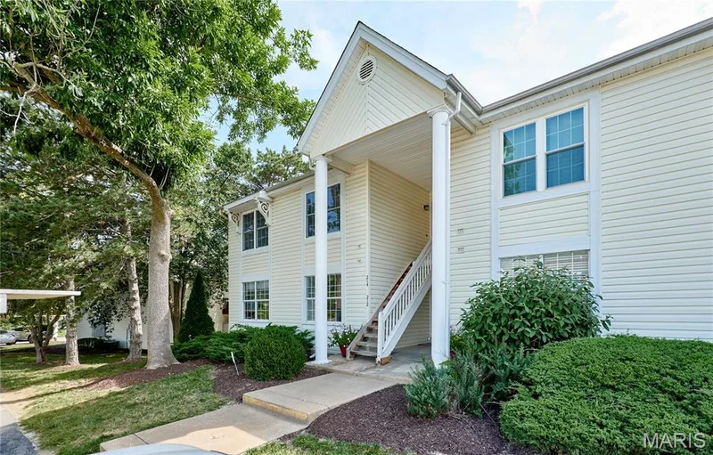 Two-story exterior with light-colored siding, a prominent gabled entrance, white column supports, and a dedicated exterior staircase — 214 Sugar Lake Drive #5, St Peters, MO 63376