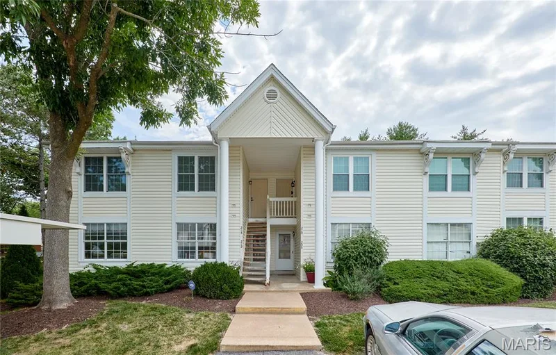 Exterior facade featuring light-colored siding, multiple windows, and a prominent entry porch with white columns — 214 Sugar Lake Drive #5, St Peters, MO 63376