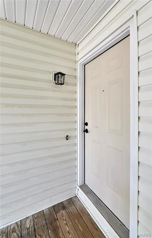 Front entry featuring a paneled door with black hardware, wood-finish flooring, white siding, and an overhead soffit — 214 Sugar Lake Drive #5, St Peters, MO 63376