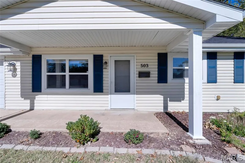 Exterior featuring light-colored horizontal siding, decorative blue shutters, a covered concrete front porch, and a columned entryway — 503 Eggering Drive, O'Fallon, MO 63366