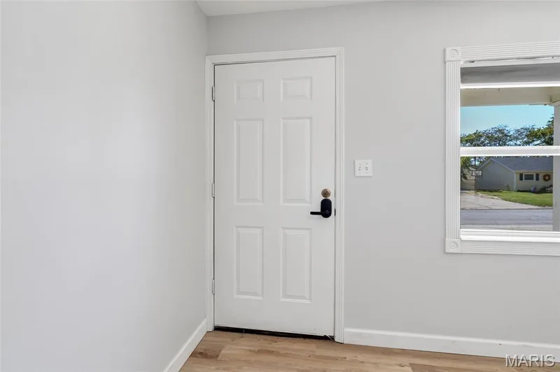 Six-panel white door with electronic deadbolt, wood-finish flooring, and single-pane window with white trim — 503 Eggering Drive, O'Fallon, MO 63366