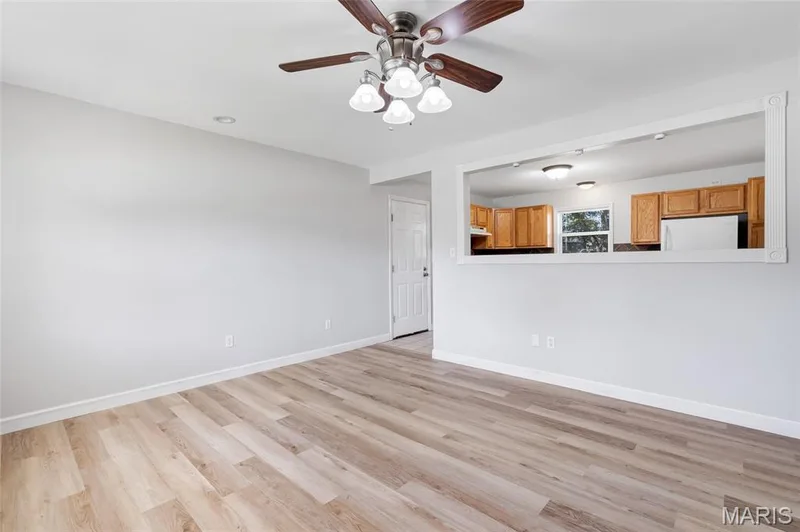 Wood-finish flooring, ceiling fan with integrated lighting, and pass-through window opening to kitchen cabinetry — 503 Eggering Drive, O'Fallon, MO 63366
