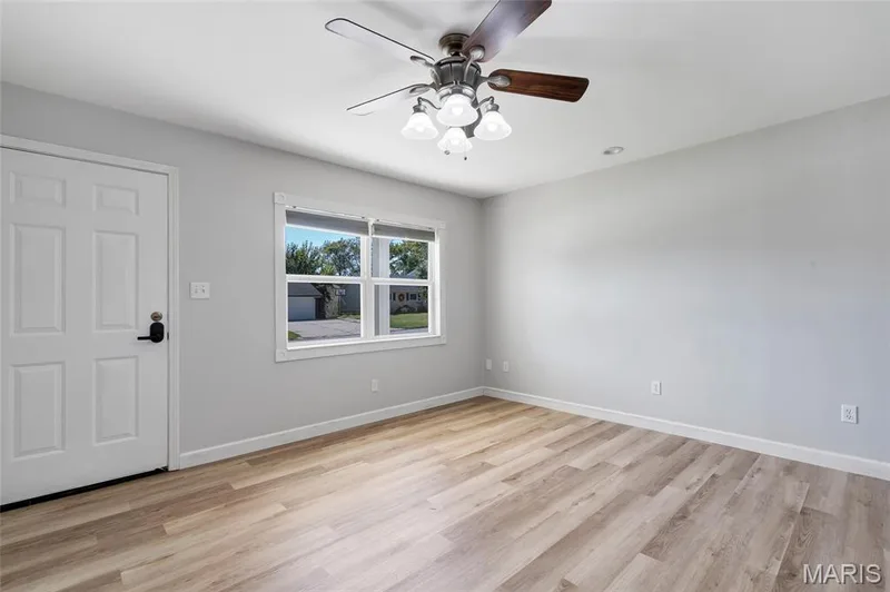 Neutral interior featuring wood-finish flooring, a multi-light ceiling fan with integrated blades, a six-panel entry door, and a dual-pane window — 503 Eggering Drive, O'Fallon, MO 63366