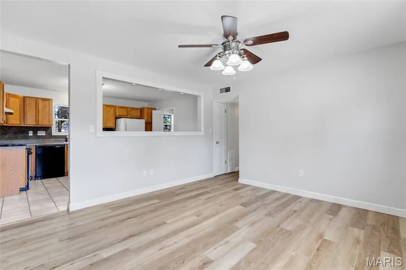 Living area featuring wood-finish flooring, a ceiling fan with integrated lighting, and a kitchen passthrough opening — 503 Eggering Drive, O'Fallon, MO 63366