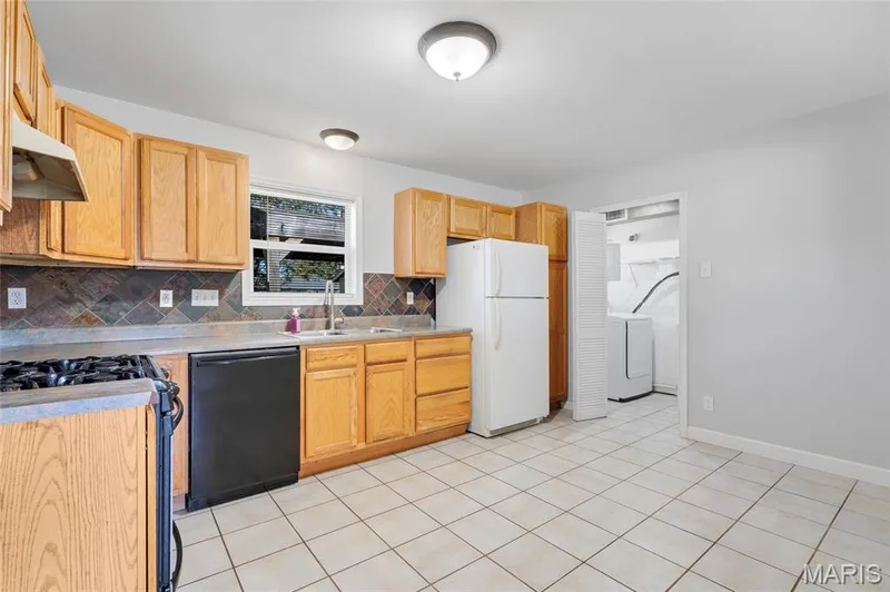 Kitchen featuring wood cabinetry, tiled backsplash, neutral tile flooring, and built-in laundry area — 503 Eggering Drive, O'Fallon, MO 63366