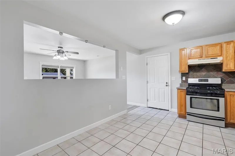 Kitchen featuring light wood cabinetry, stainless steel range, decorative tile backsplash, ceramic tile flooring, and a large wall cutout — 503 Eggering Drive, O'Fallon, MO 63366