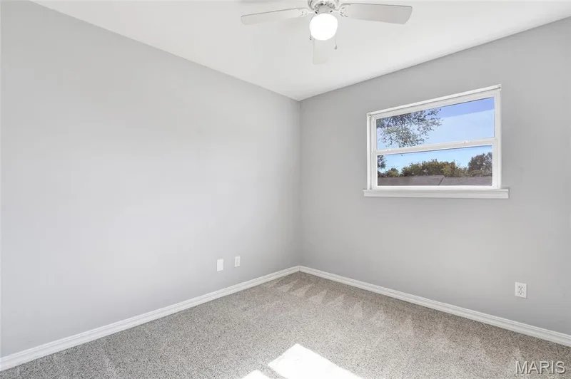 Neutral-toned interior space featuring light-colored wall paint, wall-to-wall carpeting, a single-hung window, and a ceiling-mounted fan with integrated lighting — 503 Eggering Drive, O'Fallon, MO 63366