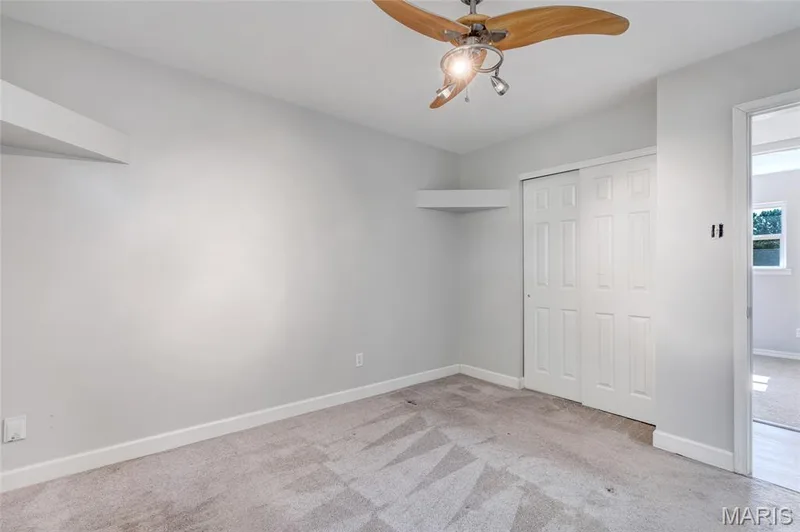 Interior room featuring neutral wall paint, carpeted flooring, built-in corner shelving, a sliding-door closet, and a ceiling fan with integrated lighting — 503 Eggering Drive, O'Fallon, MO 63366