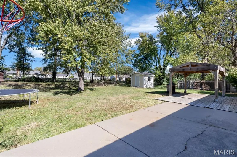 Backyard featuring a concrete patio, wooden pergola, detached storage shed, mature trees, and fenced perimeter — 503 Eggering Drive, O'Fallon, MO 63366