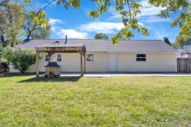 Backyard featuring a concrete patio, a covered wooden pergola, a stone-base outdoor fireplace, and a manicured lawn — 503 Eggering Drive, O'Fallon, MO 63366