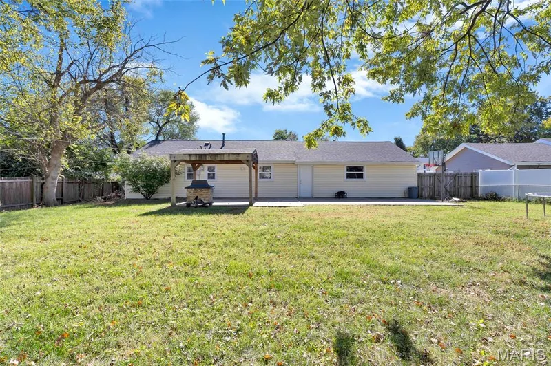 Expansive backyard featuring a sprawling lawn, mature trees, a paved concrete patio, a wooden pergola, and perimeter wood fencing — 503 Eggering Drive, O'Fallon, MO 63366