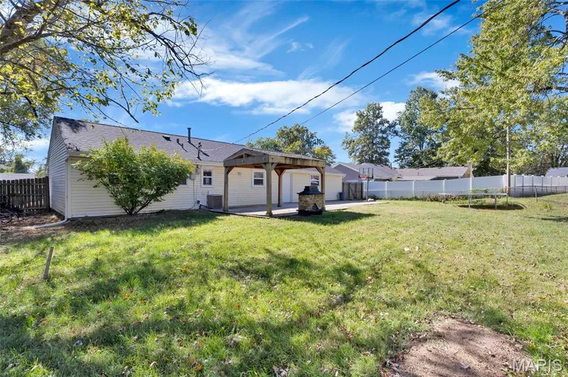 Spacious backyard featuring a wood-frame pergola, stone-clad outdoor fireplace, perimeter vinyl fencing, and mature trees — 503 Eggering Drive, O'Fallon, MO 63366