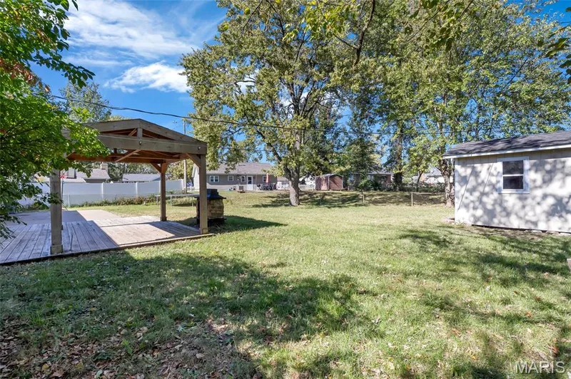 Backyard featuring a wood-frame covered patio, detached storage structure, mature trees, and perimeter fencing — 503 Eggering Drive, O'Fallon, MO 63366